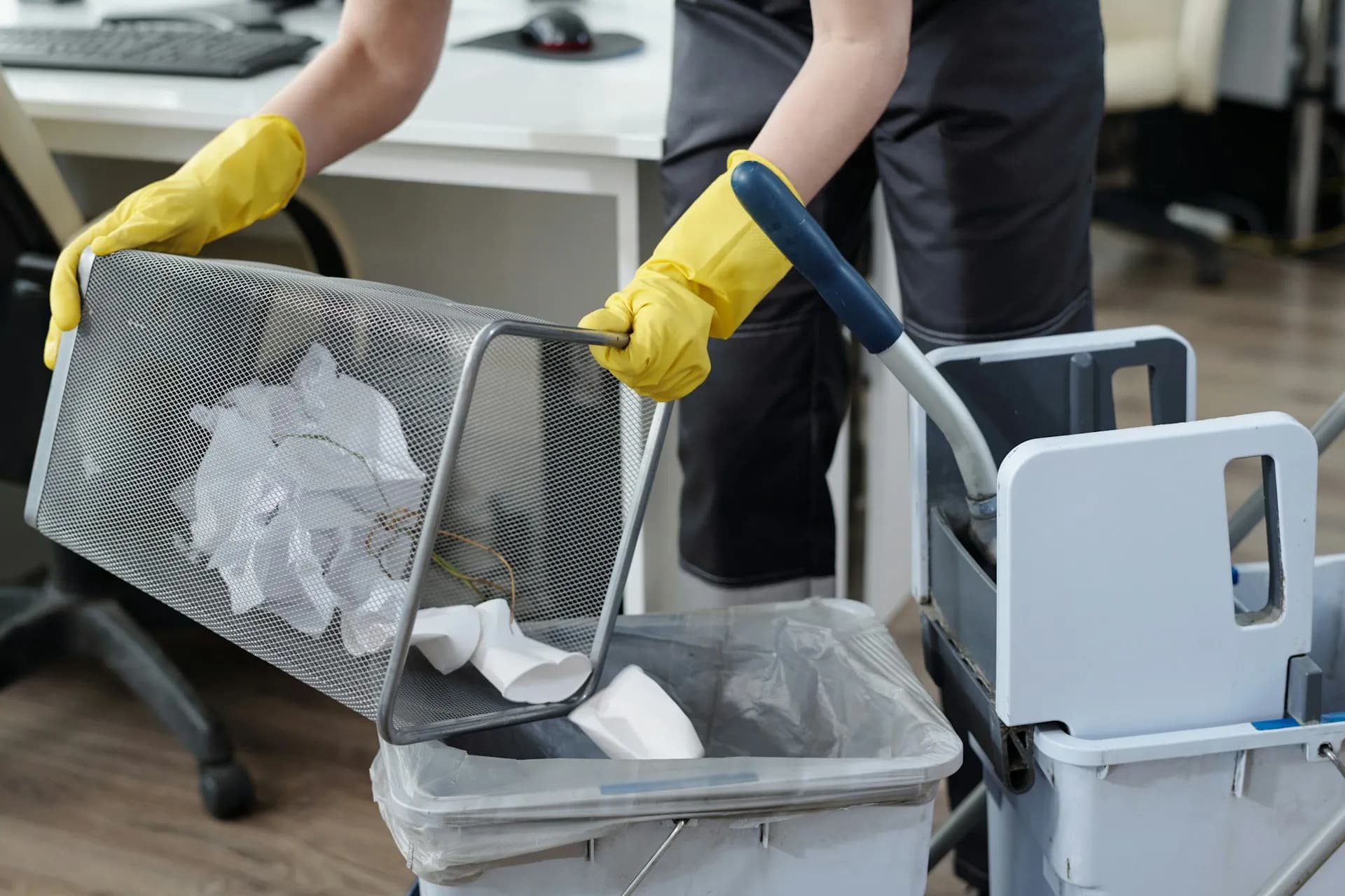 Reinigungskraft leert einen Papierkorb in einen Reinigungswagen in einem Büro.